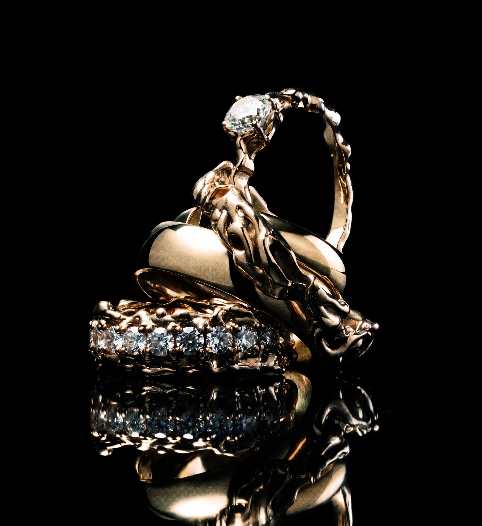 Yellow gold wedding bands with a molten, lava-like texture, set with salt and pepper diamonds and stacked against black